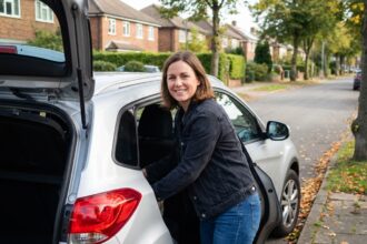 Femme souriante à côté d'un SUV dans un quartier résidentiel